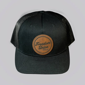 Black cap with a leather patch featuring 'Freedom Union' on a light gray background